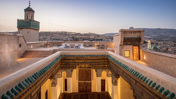 A rooftop terrace with a view of a cityscape, a tower, and a traditional building with a wooden door. - Dar Bensouda (Fes)