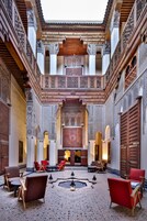 Un patio con elaborados trabajos en azulejos, un espacio central con asientos y sillas rojas, y un techo de madera.