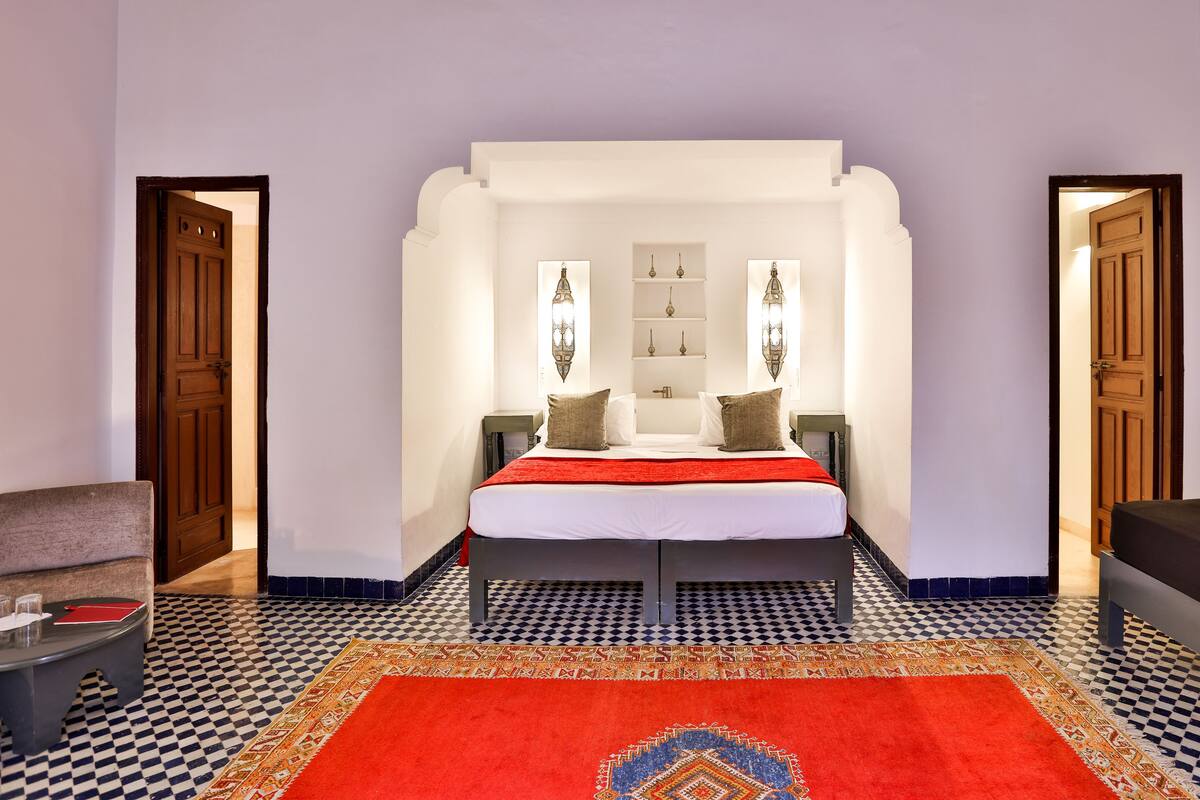 A bedroom with a bed, two nightstands, a red rug, and a checkered floor.