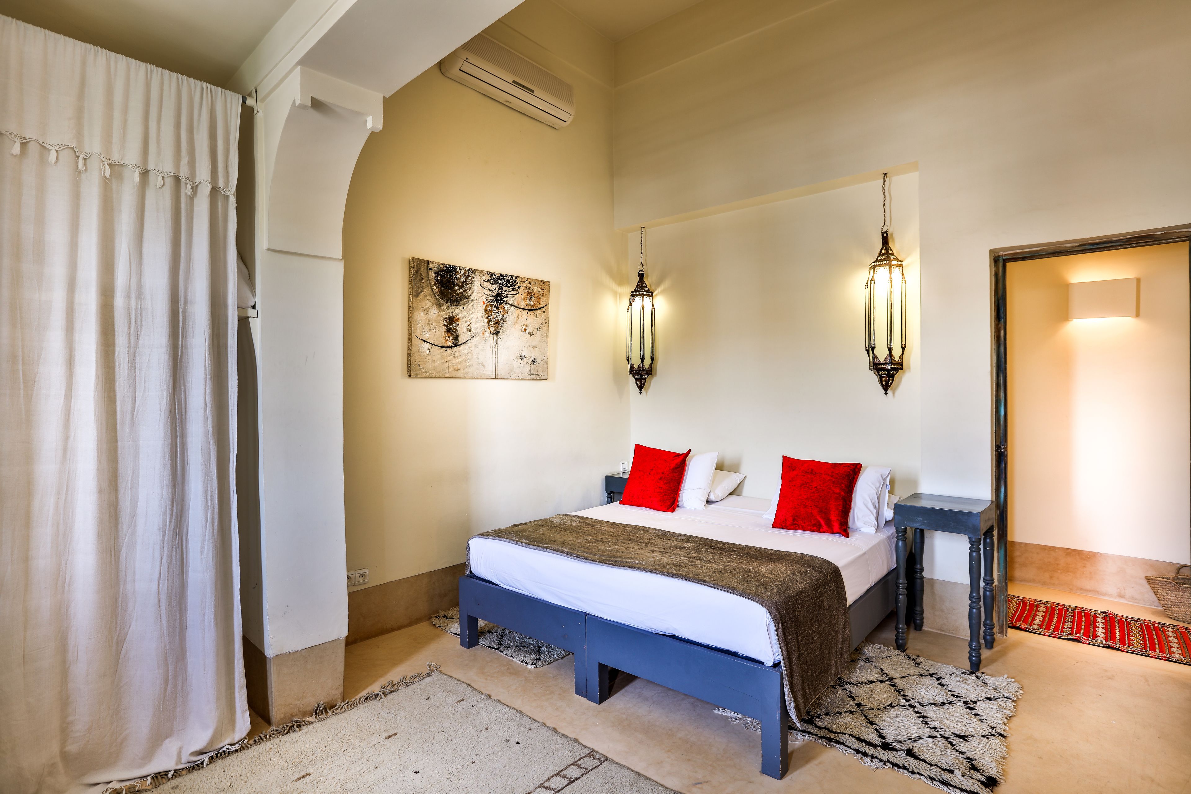 A bedroom with a bed, bedside tables, a nightstand, a wall-mounted artwork, and a door leading to another room.