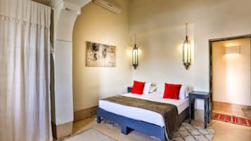 A bedroom with a bed, bedside tables, a nightstand, a wall-mounted artwork, and a door leading to another room.