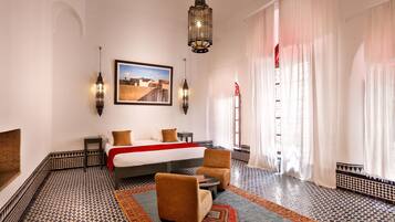 Habitación de hotel con cama, dos sillas, una mesita pequeña, piso estampado y un cuadro en la pared.