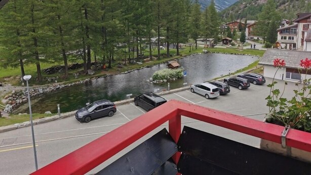 A view of a parking area with cars, a small lake, and a mountainous backdrop. - Hotel Restaurant Mattmarkblick (Saas Almagell)