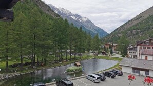A parking area with several cars, a small building, and a river with mountains in the background. - Hotel Restaurant Mattmarkblick (Saas Almagell)