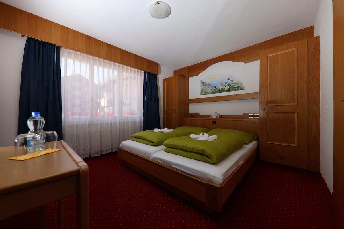 A hotel room with a wooden bed, a desk with a water bottle, and a painting on the wall.