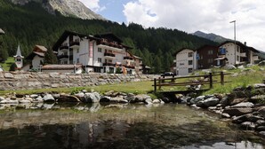 A mountain resort with a clear pond, wooden bridge, and buildings with balconies. - Hotel Restaurant Mattmarkblick (Saas Almagell)