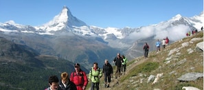 A group of hikers on a mountain trail with a snow-capped peak in the background. - Hotel Restaurant Mattmarkblick (Saas Almagell)