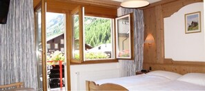 Quarto com cama, poltrona e janela com vista para uma montanha e um edifício.