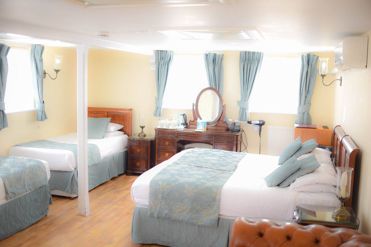 Ein Hotelzimmer mit zwei Betten, einem hölzernen Schminktisch, einem Spiegel, einem Schreibtisch und einem Stuhl.