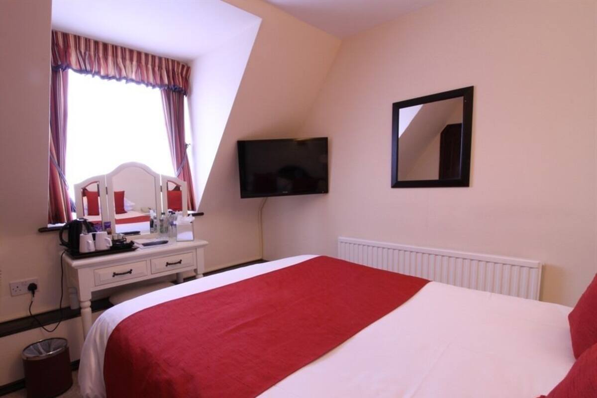 Ein Hotelzimmer mit Bett, Schreibtisch mit Computer, Fernseher und einem Fenster mit Vorhängen.