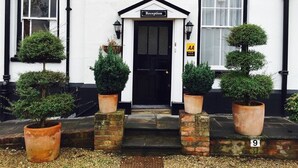 A reception area with a black door, a sign above the door, and potted plants on either side of the entrance. - Castle House Hotel (Canterbury)