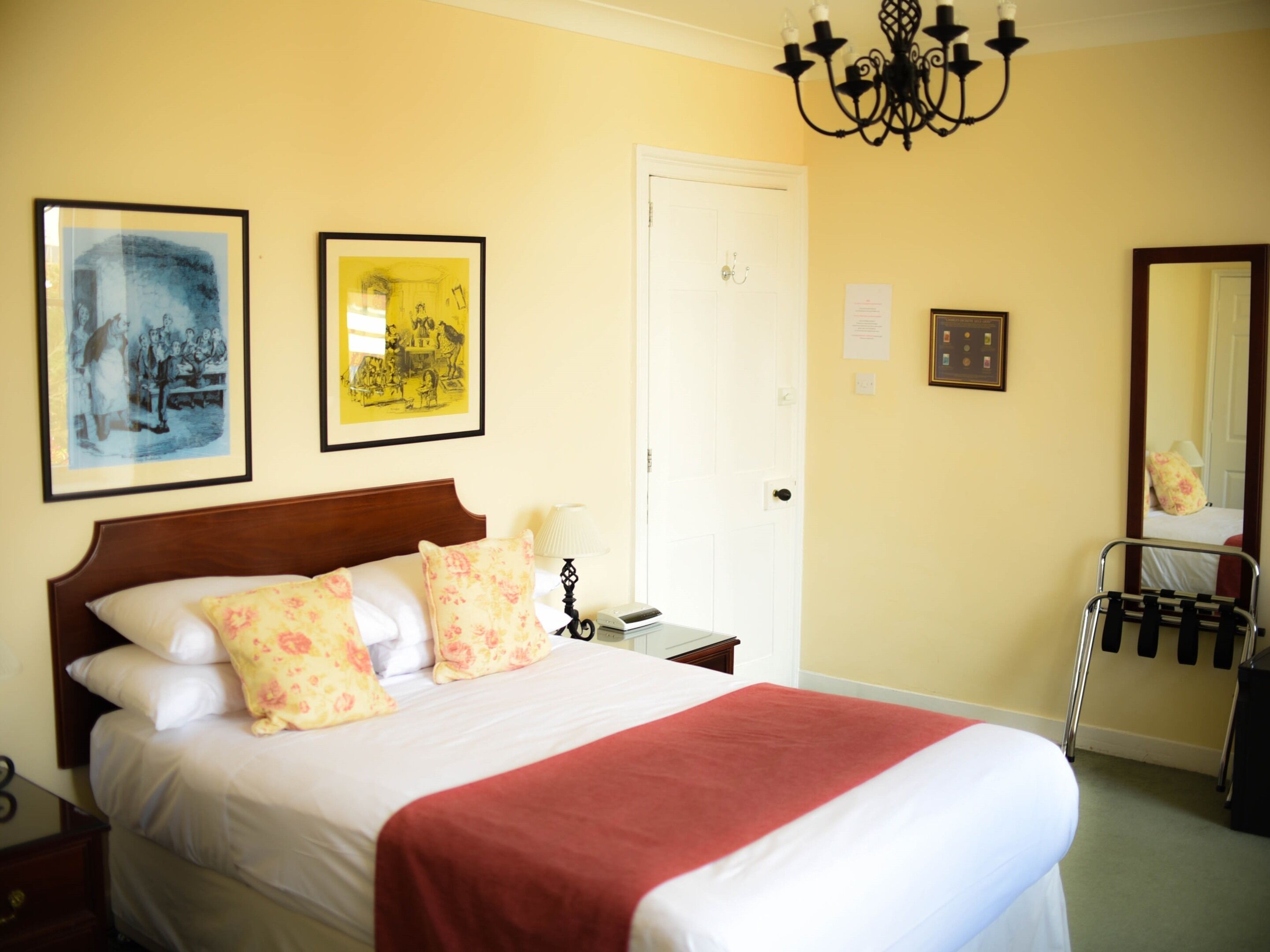 Habitación de hotel con cama, mesita de noche, lámpara, silla y dos cuadros en la pared.