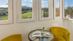 A room with a glass table, two yellow chairs, and a view of a green landscape through large windows. - Point de Vue (Rabat)