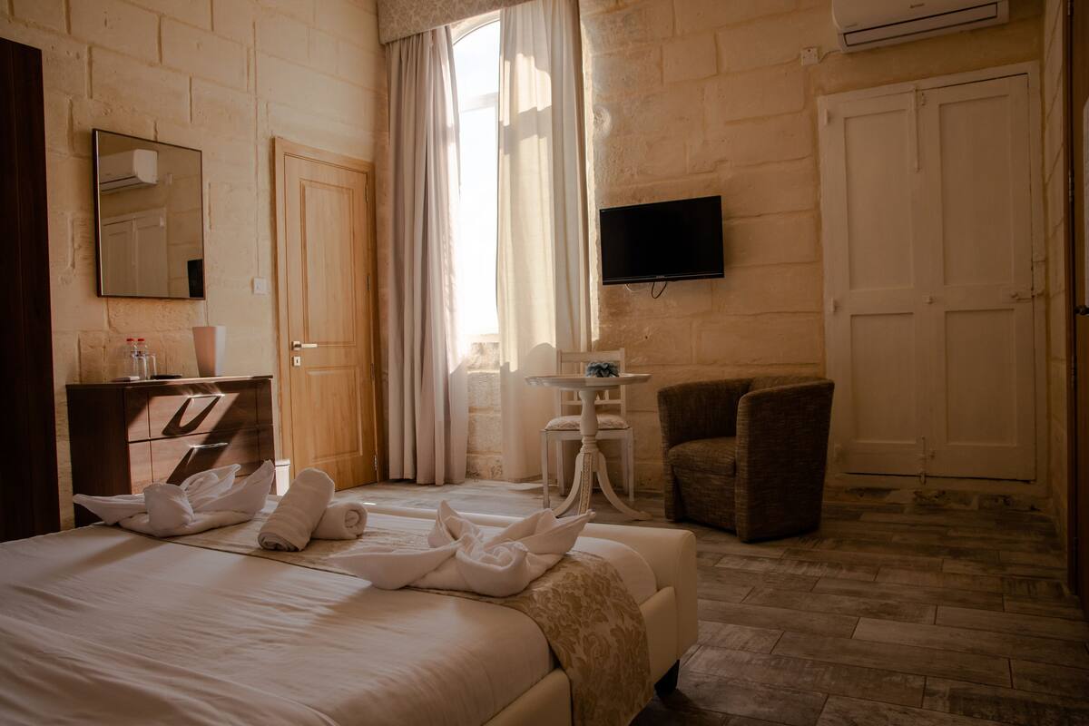 A hotel room with a bed, a desk, a chair, a television, and a window with curtains.