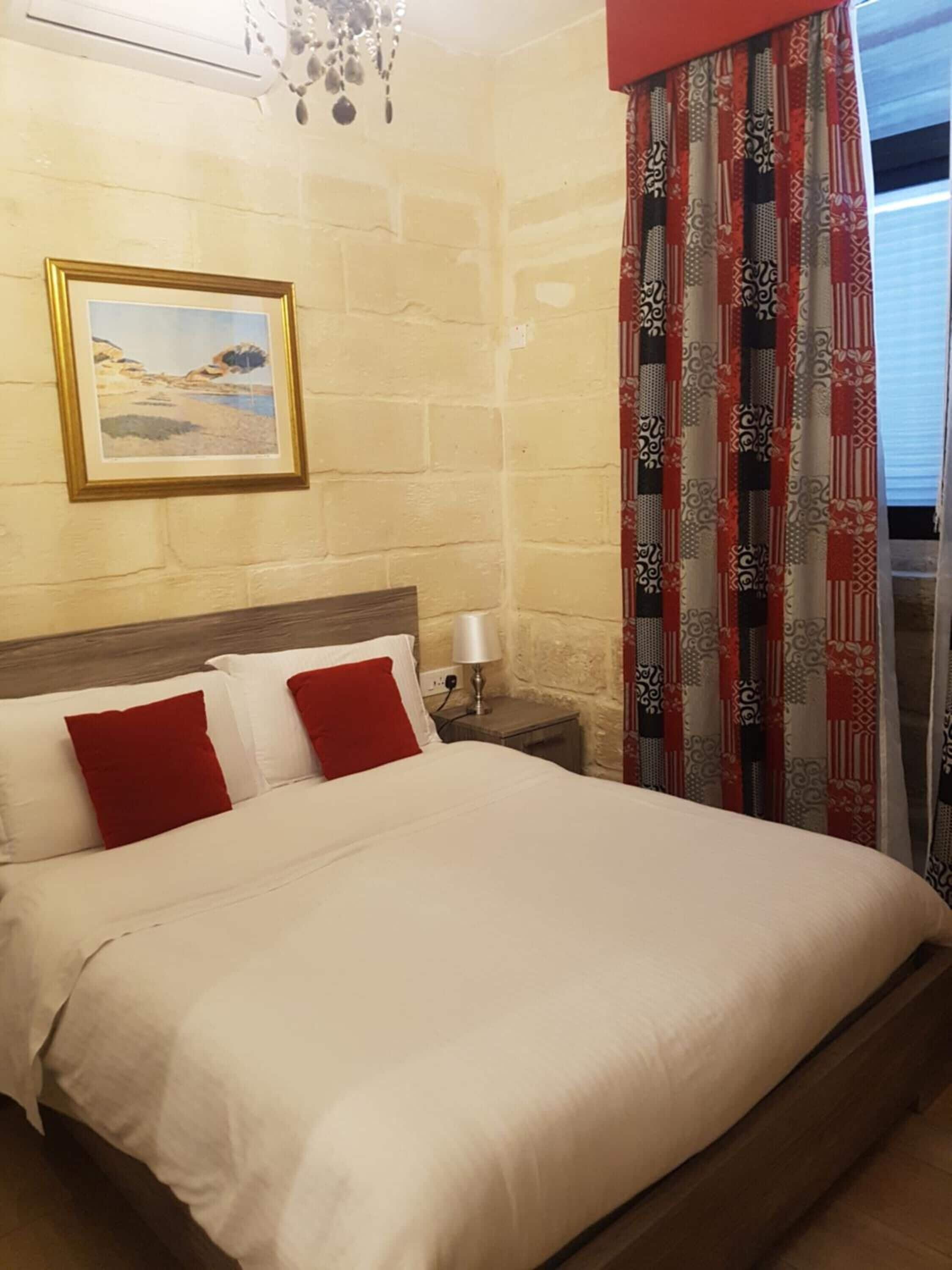 A hotel room with a bed, a nightstand, a lamp, a painting, and patterned curtains.