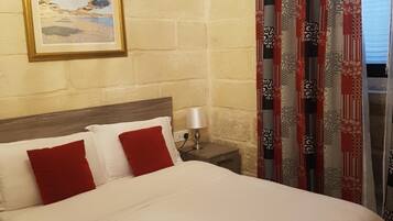 A hotel room with a bed, a nightstand, a lamp, a painting, and patterned curtains.