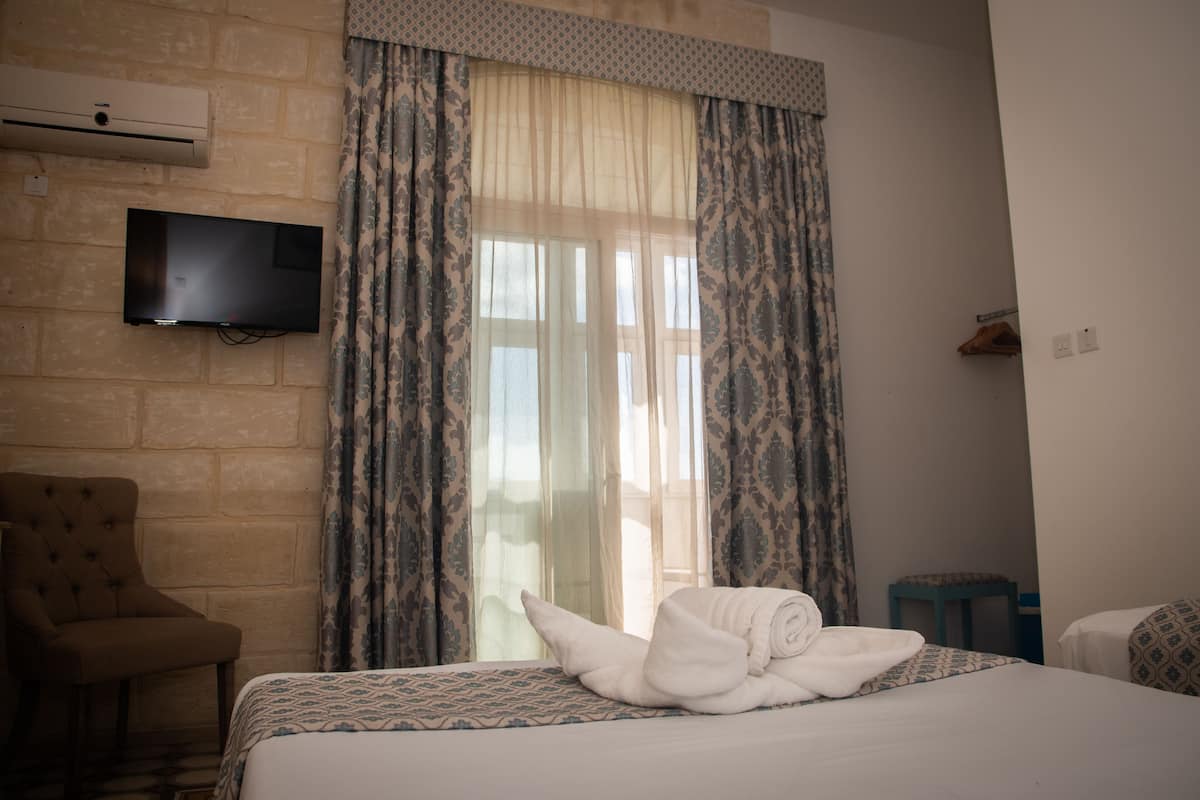 A hotel room with a bed, a television mounted on the wall, a chair, and a window with curtains.