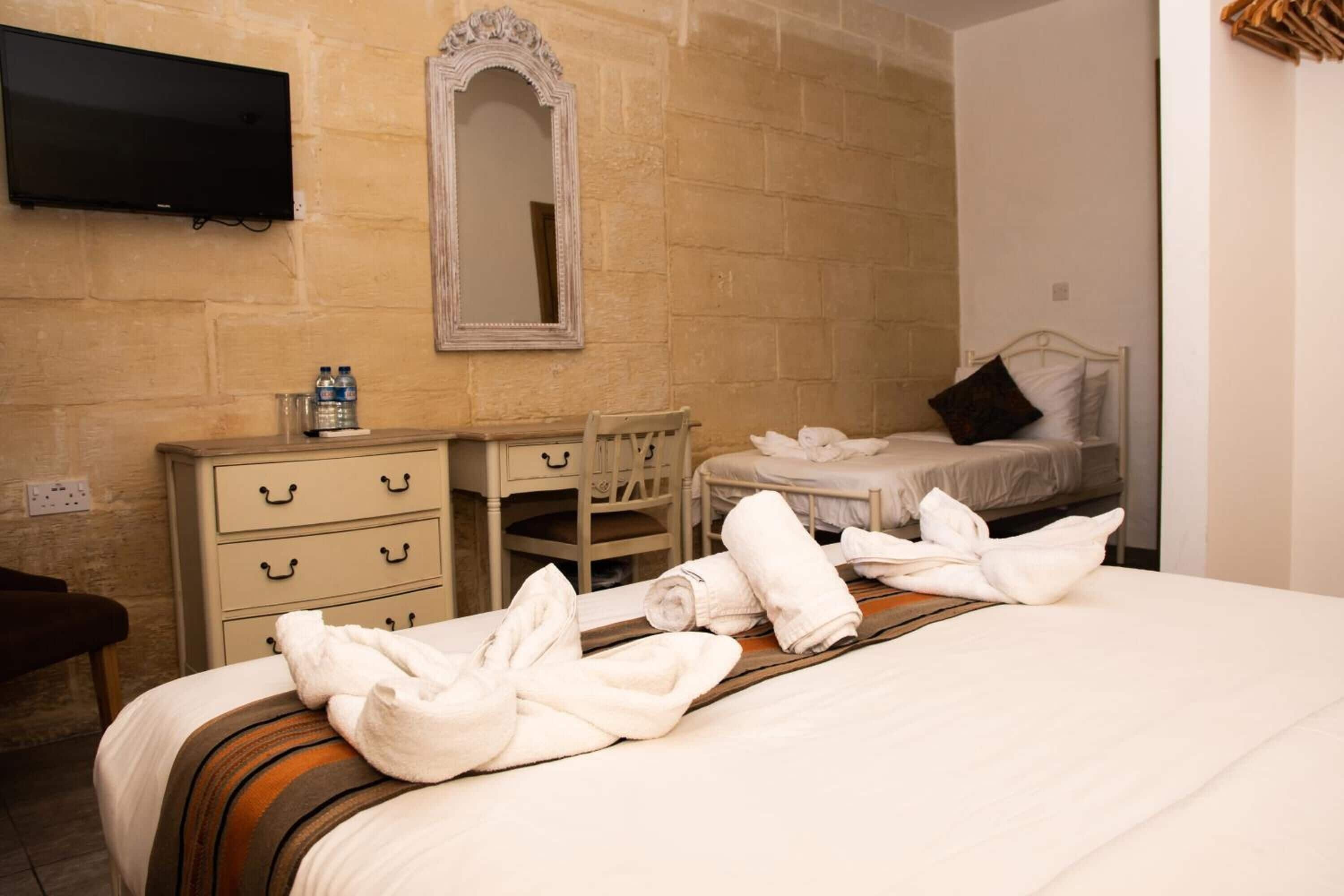 Habitación de hotel con una cama grande, una mesita de noche con artículos de aseo, un espejo y un televisor montado en la pared.