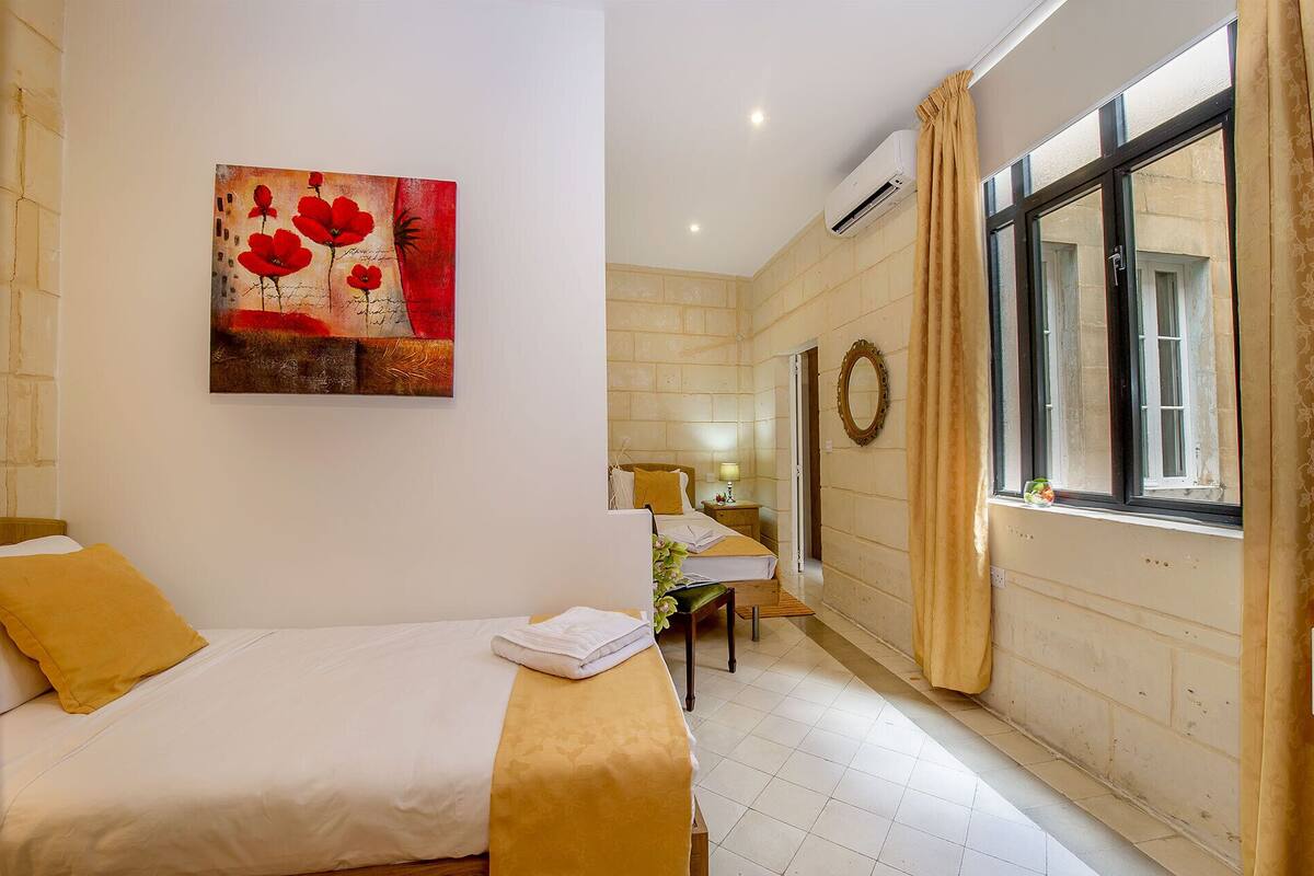 A hotel room with a bed, a bedside table, a lamp, a mirror, and a window with curtains.
