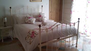 A bedroom with a checkered floor, a bed with floral bedding, a nightstand, a lamp, and two framed pictures on the wall.