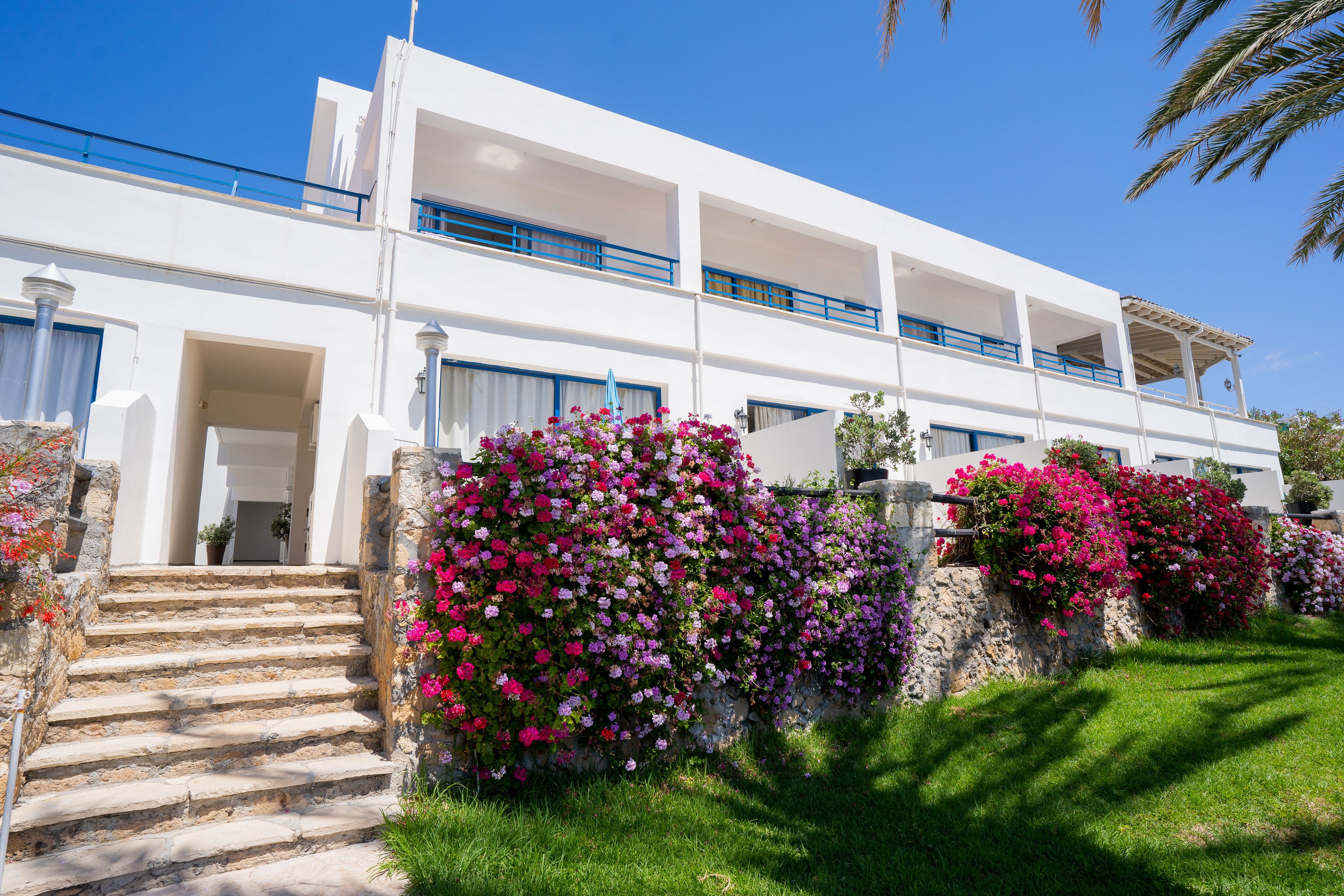 A white building with a balcony, stone steps, and vibrant flower walls.
