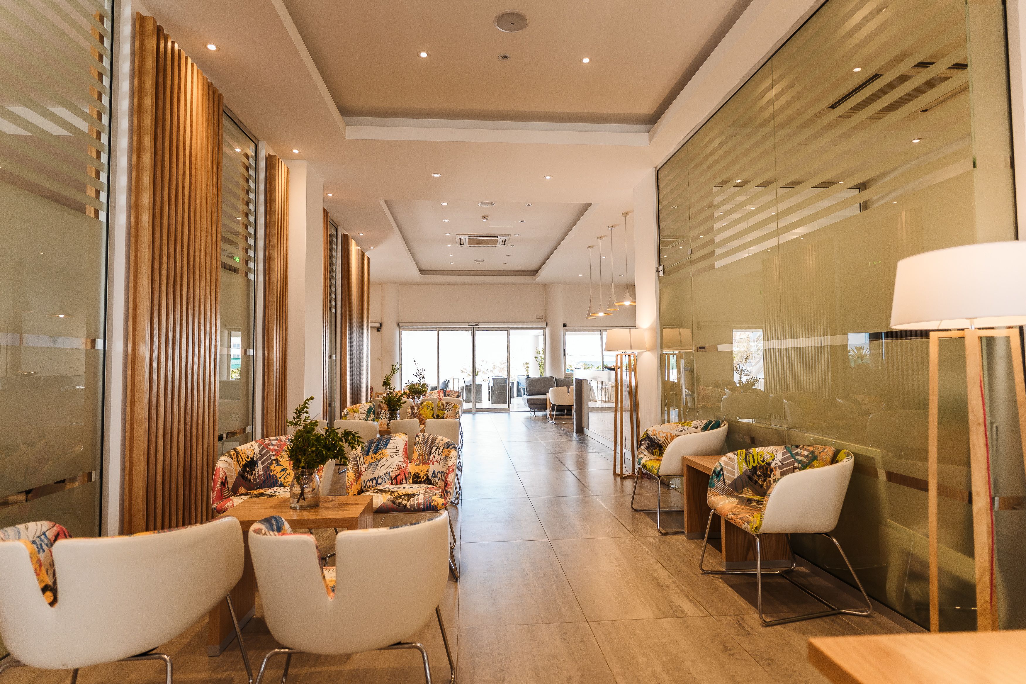 Eine moderne Hotellobby mit einer langen Rezeption, weißen Stühlen und einem großen Fenster mit Blick ins Freie.