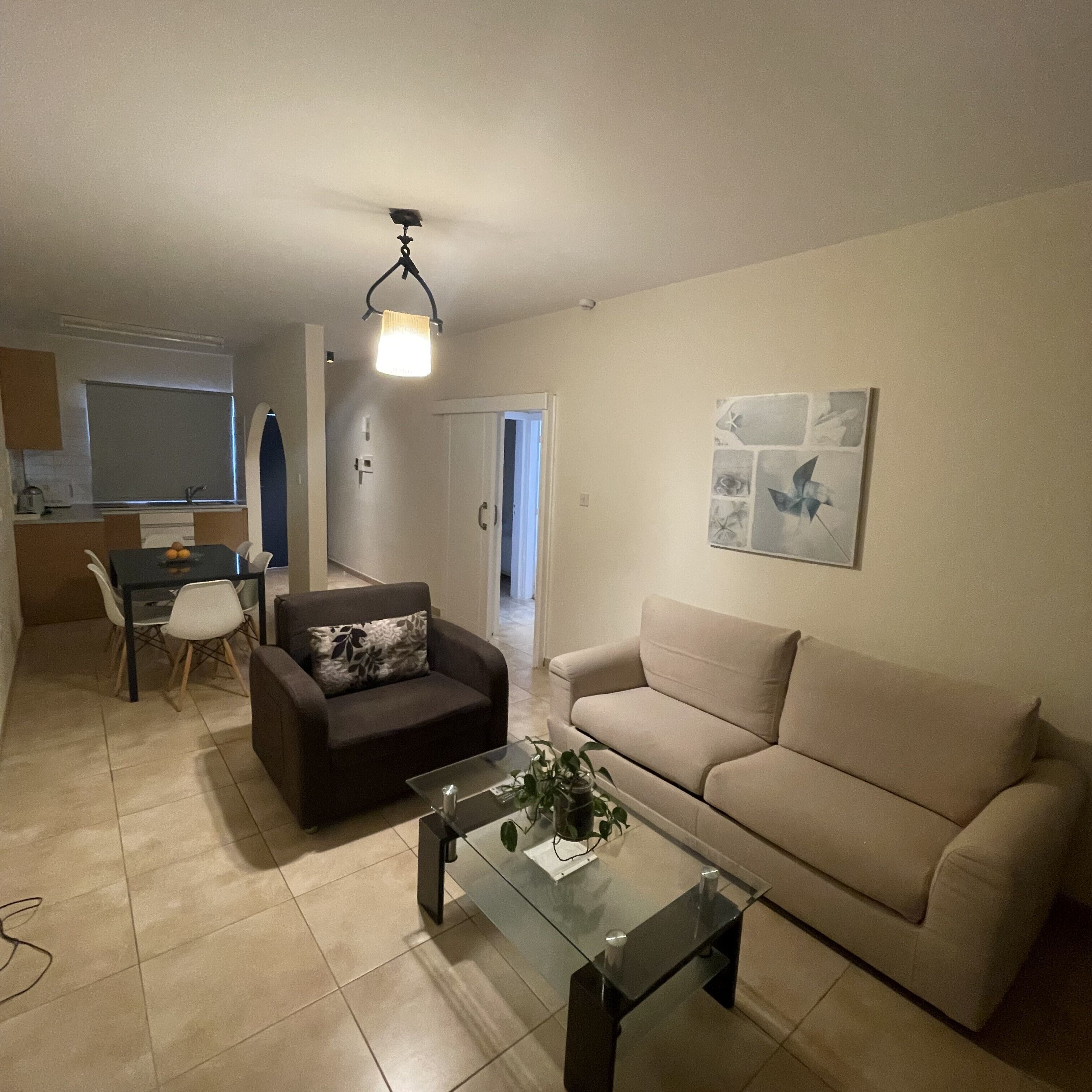 A living room with a sofa, a glass coffee table, and a dining area with a table and chairs.