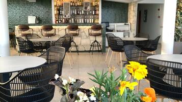 A bar area with a stone counter and black chairs. There are tables with chairs around.