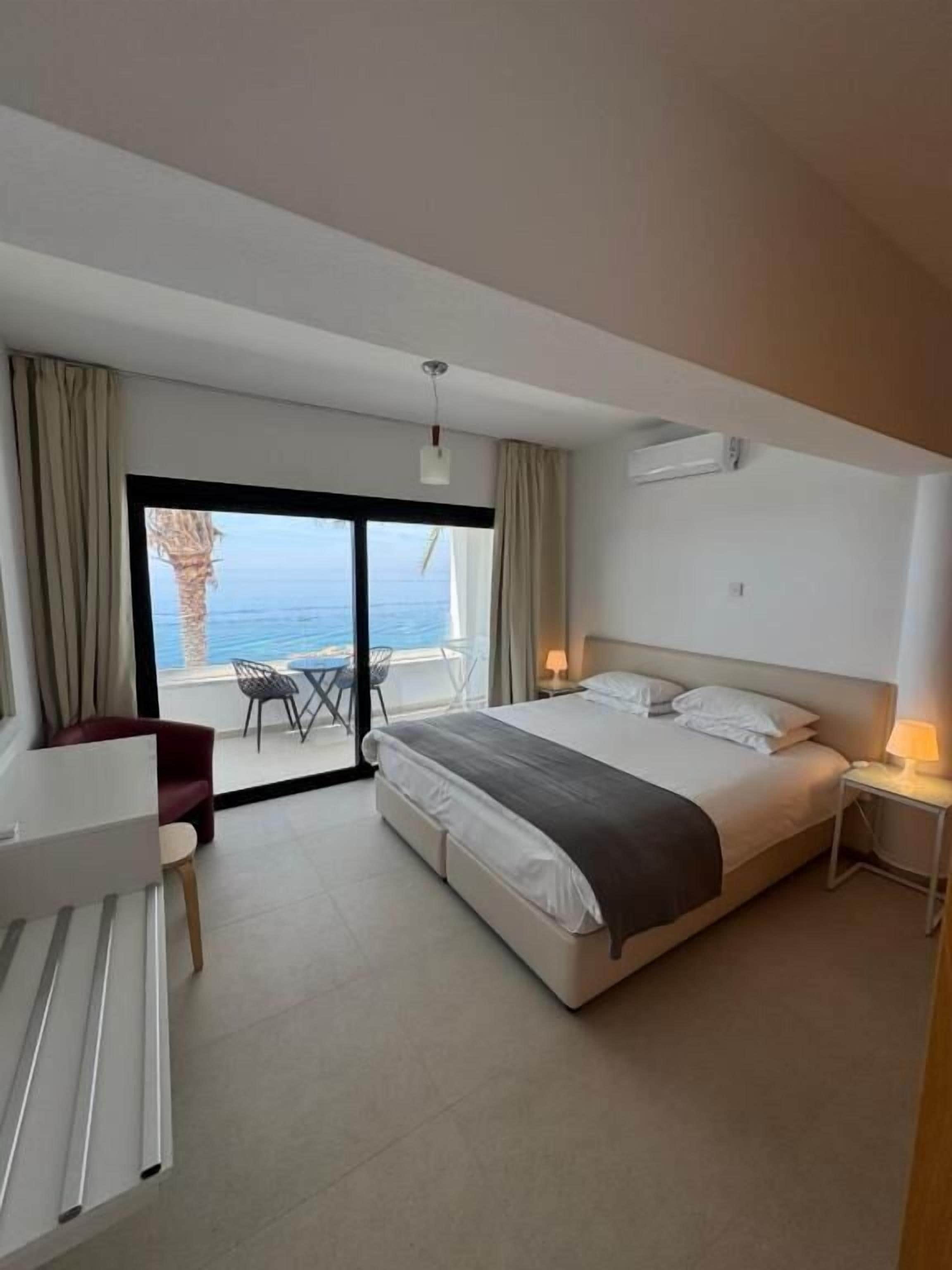 A modern hotel room with a large bed, a desk, and a view of the ocean.