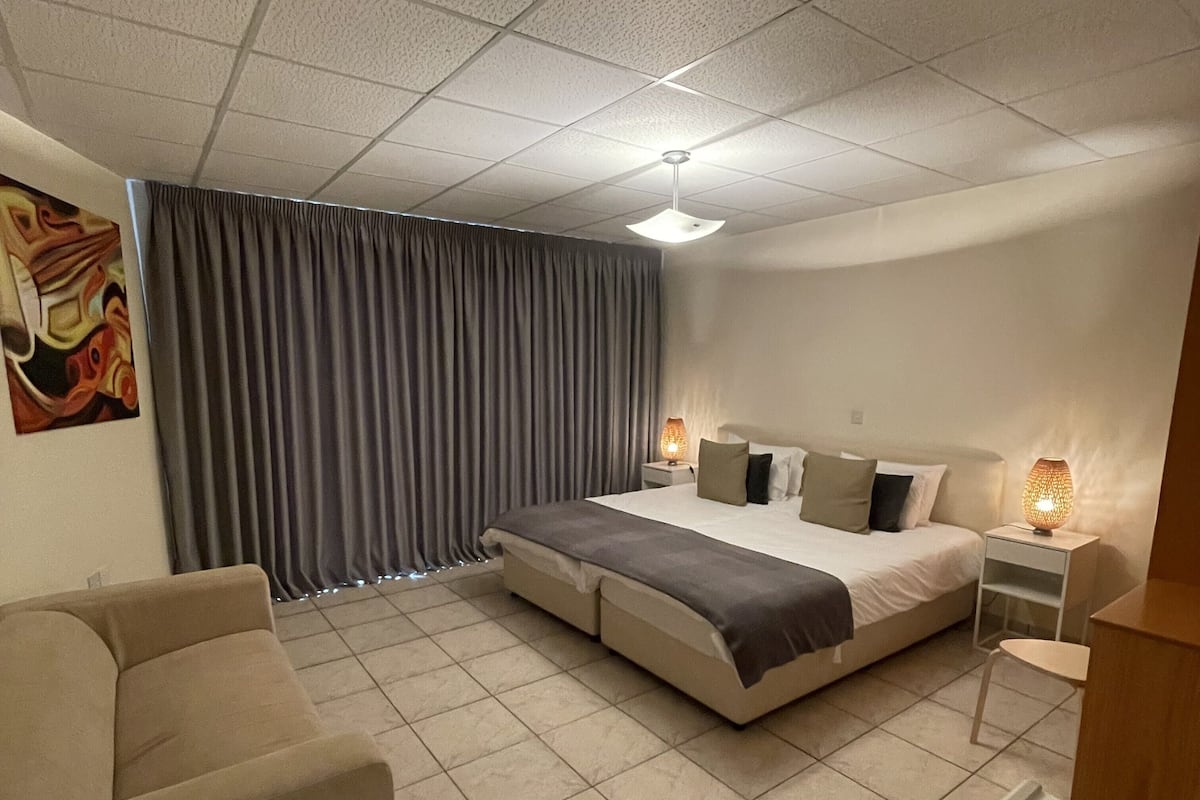 A modern hotel room with a bed, a sofa, a desk, a lamp, and a painting on the wall.