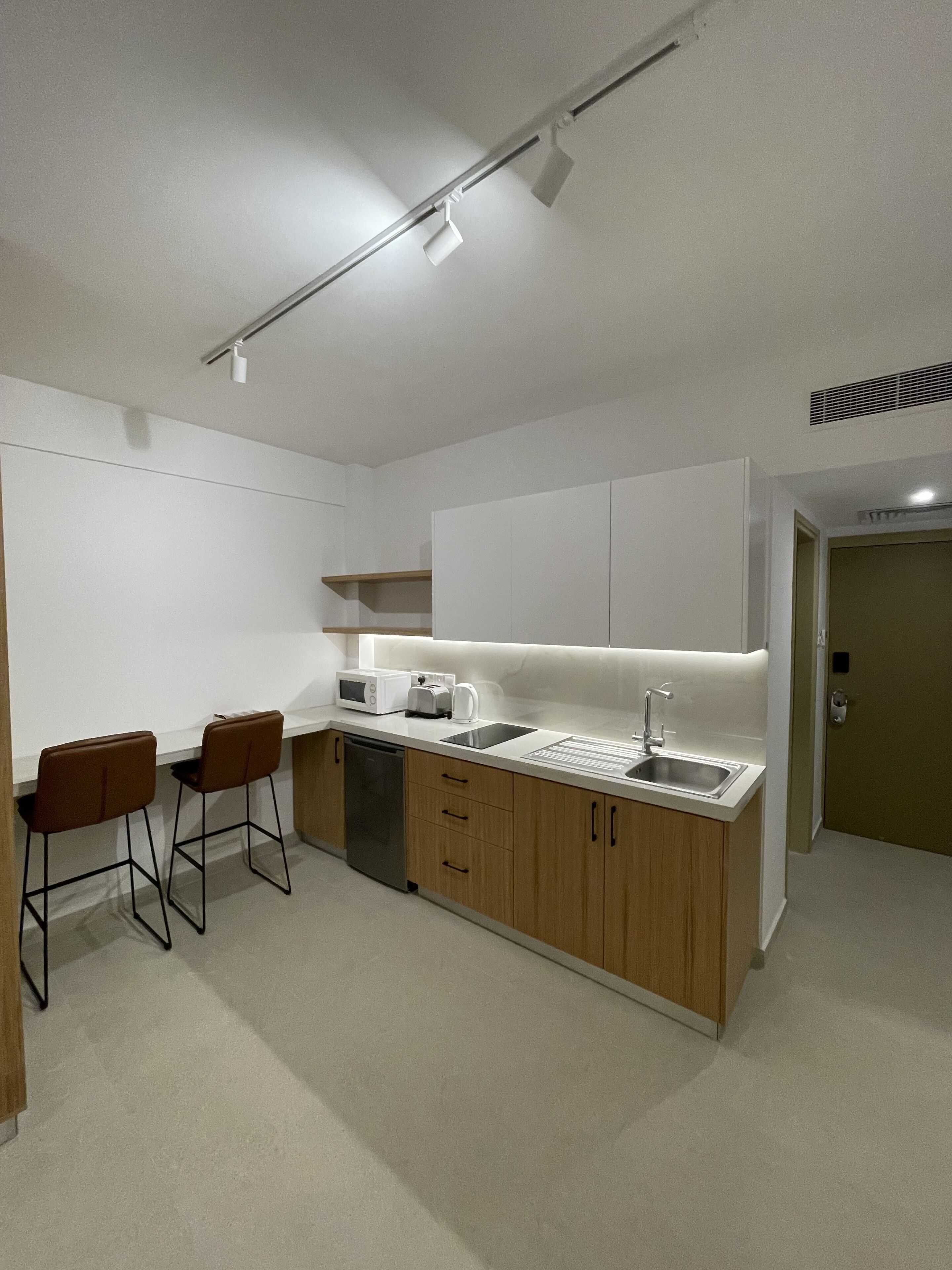 A modern kitchen with a central island, two bar stools, a dishwasher, and a sink.
