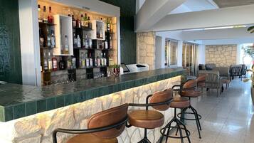 A bar area with a stone counter, multiple liquor bottles, and leather bar stools.