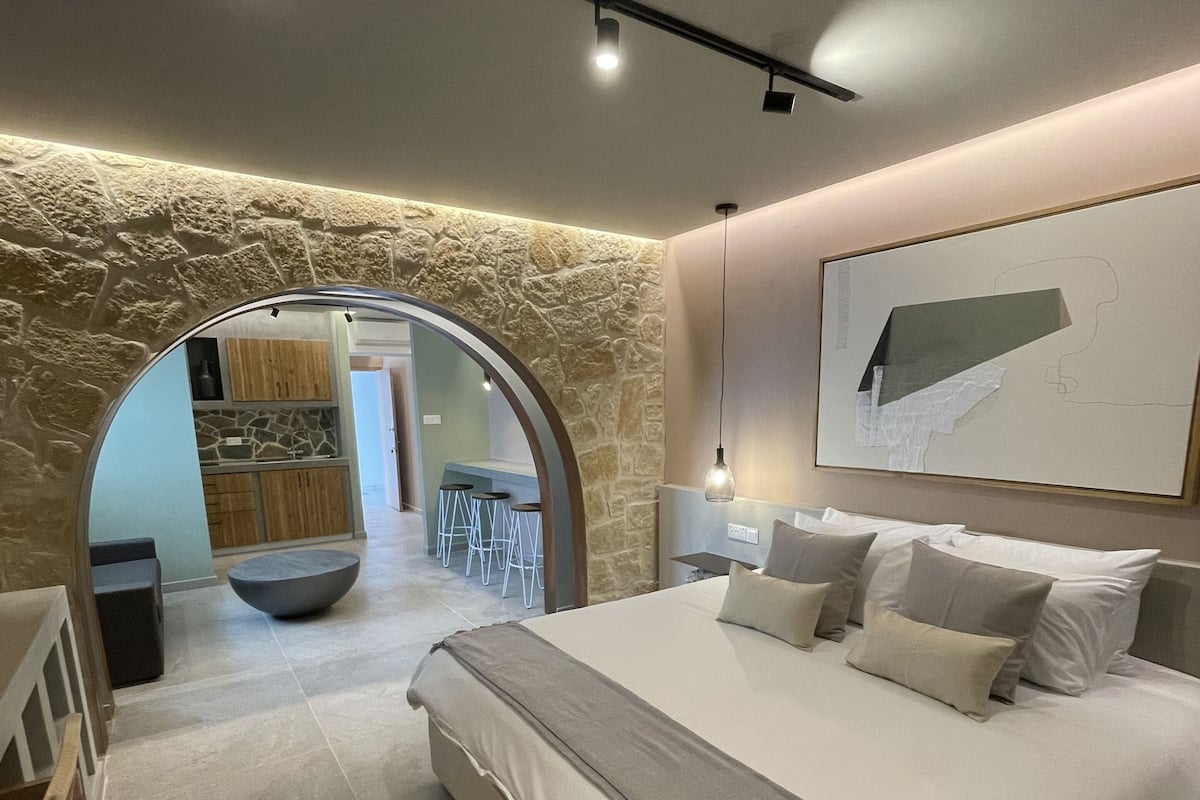 A modern bedroom with a large bed, a stone wall, and a view into another room.