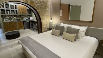 Une chambre moderne avec un grand lit, un mur d’accent en pierre, un coin cuisine et un grand miroir.