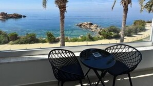 Een balkon met twee zwarte stoelen en een kleine tafel, met uitzicht op een strand met palmbomen en de zee.