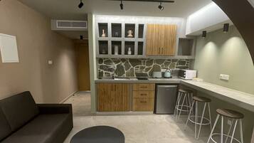 Een moderne keuken met een achterwand van steen, houten kastjes en een zwart poefje. Er is een bar met krukken en een ingebouwde oven.
