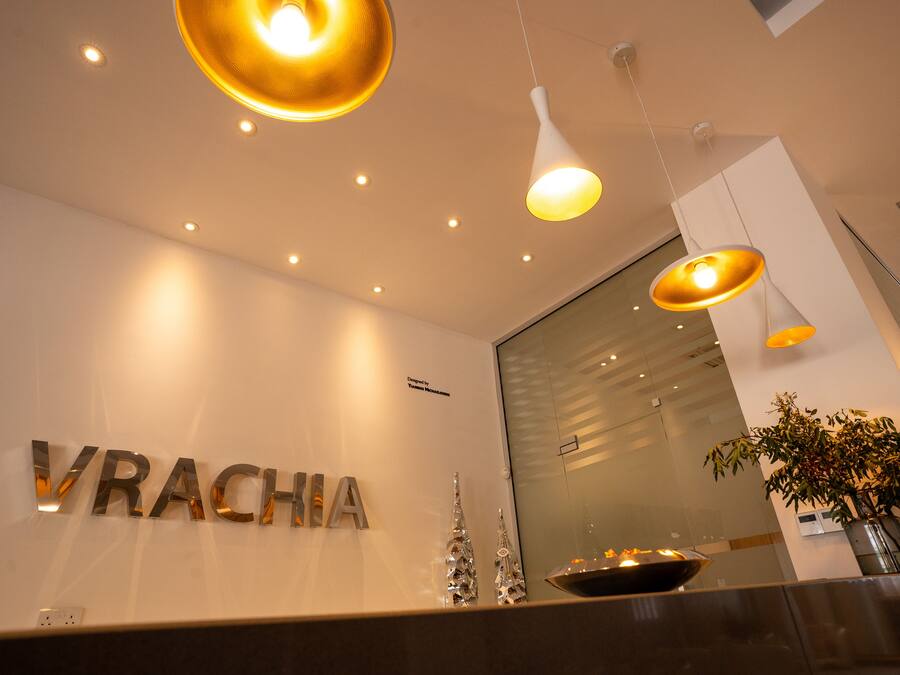 Un'area reception dal design moderno, con una scrivania, una segnaletica con il nome 'VRACHA' e elementi decorativi come un piccolo albero di Natale e un candelotto.