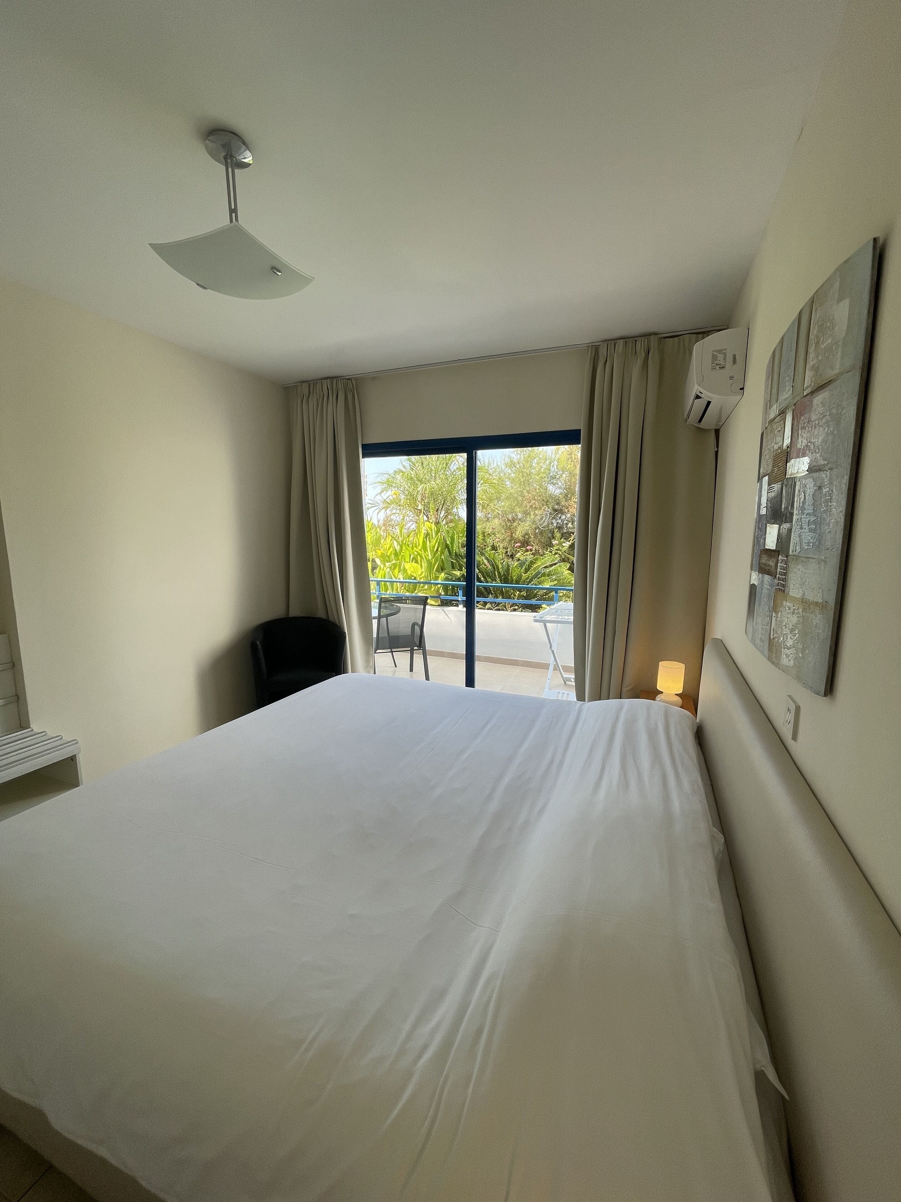 Habitación de hotel con una cama grande, ventilador de techo, vista al exterior y aire acondicionado de pared.