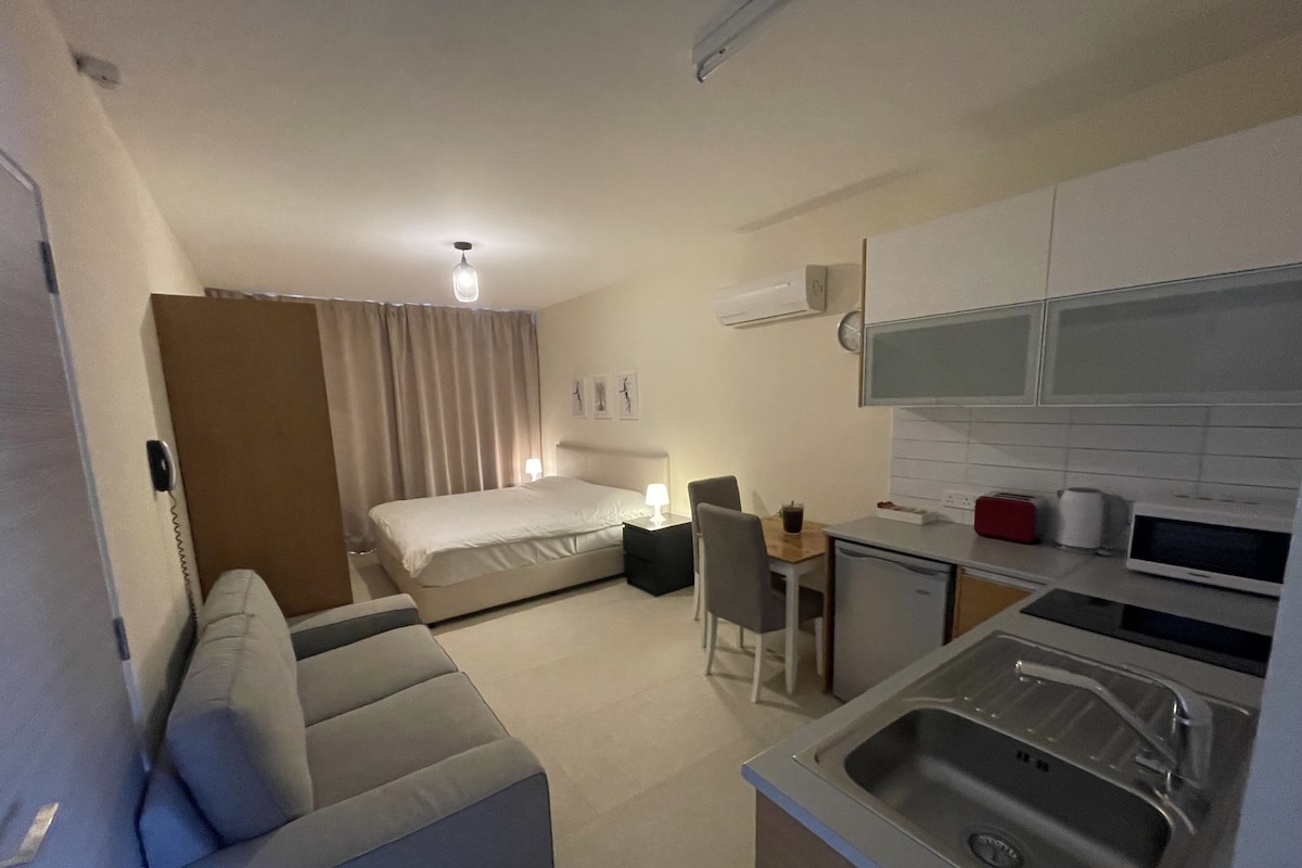A compact hotel room with a bed, a small kitchenette, a dining area, and a sofa.