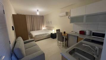 A compact hotel room with a bed, a small kitchenette, a dining area, and a sofa.