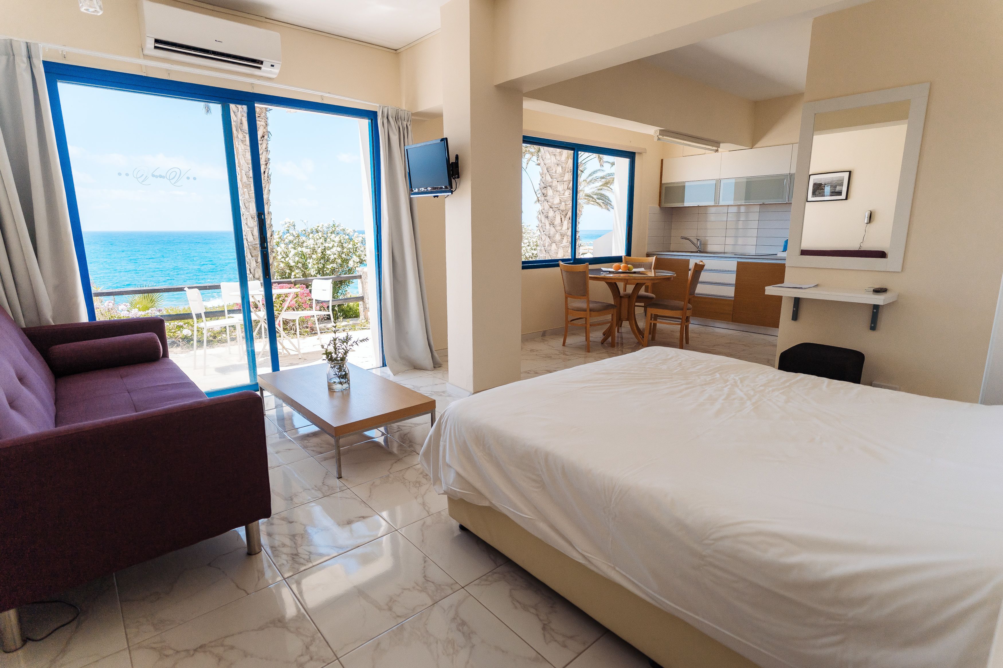 A hotel room with a bed, a sofa, a dining table, and a kitchen area.