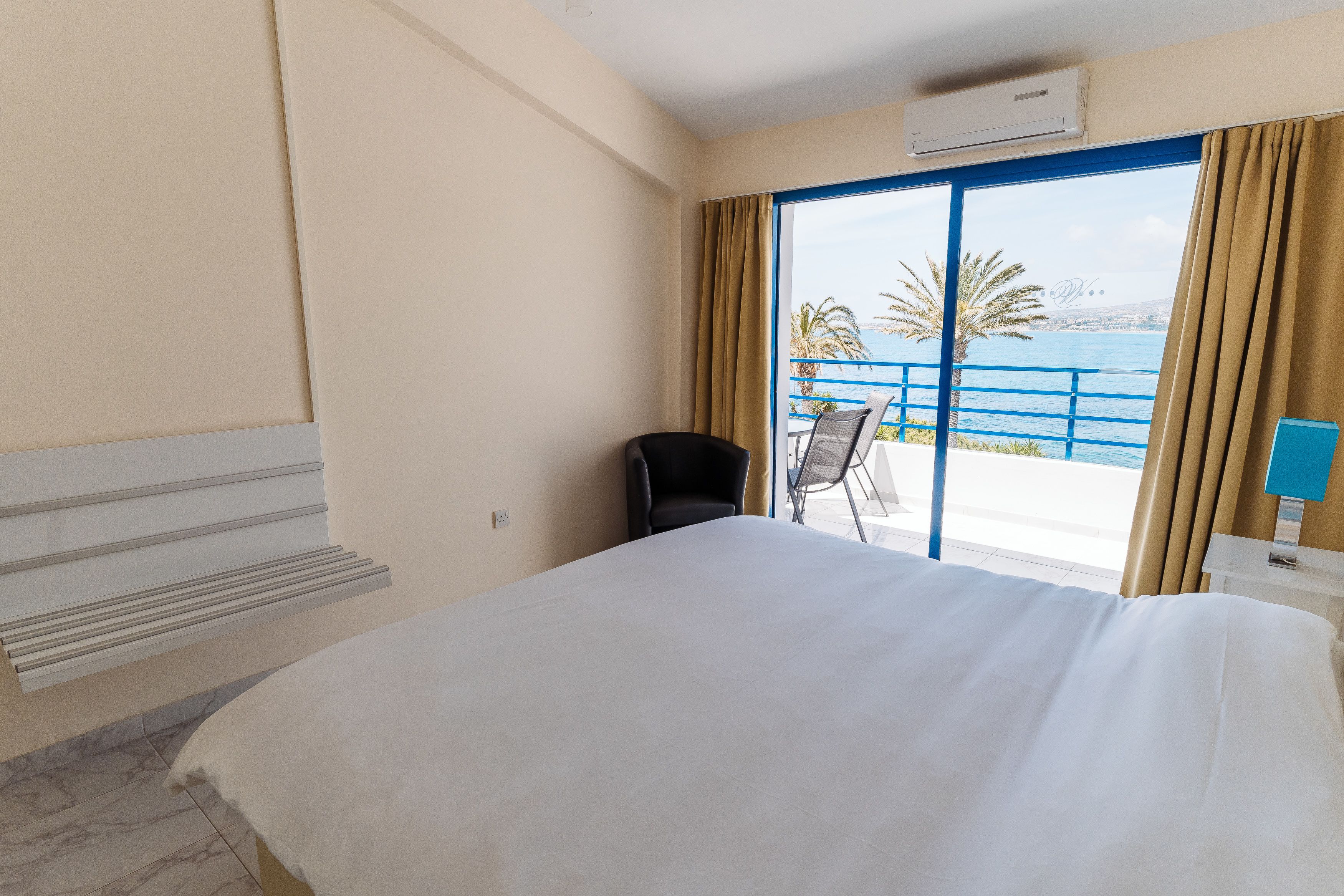 Habitación de hotel con cama, una silla, escritorio y vista al mar a través de un ventanal grande.