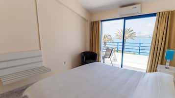 Habitación de hotel con cama, una silla, escritorio y vista al mar a través de un ventanal grande.