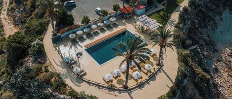Eine Luftaufnahme eines Resorts mit Schwimmbad, Liegestühlen und Palmen.