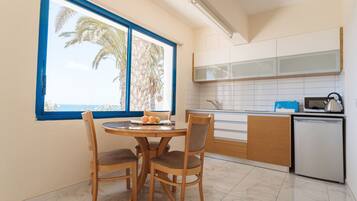 A modern kitchen with a dining area, a window with a view of palm trees, and a small refrigerator.