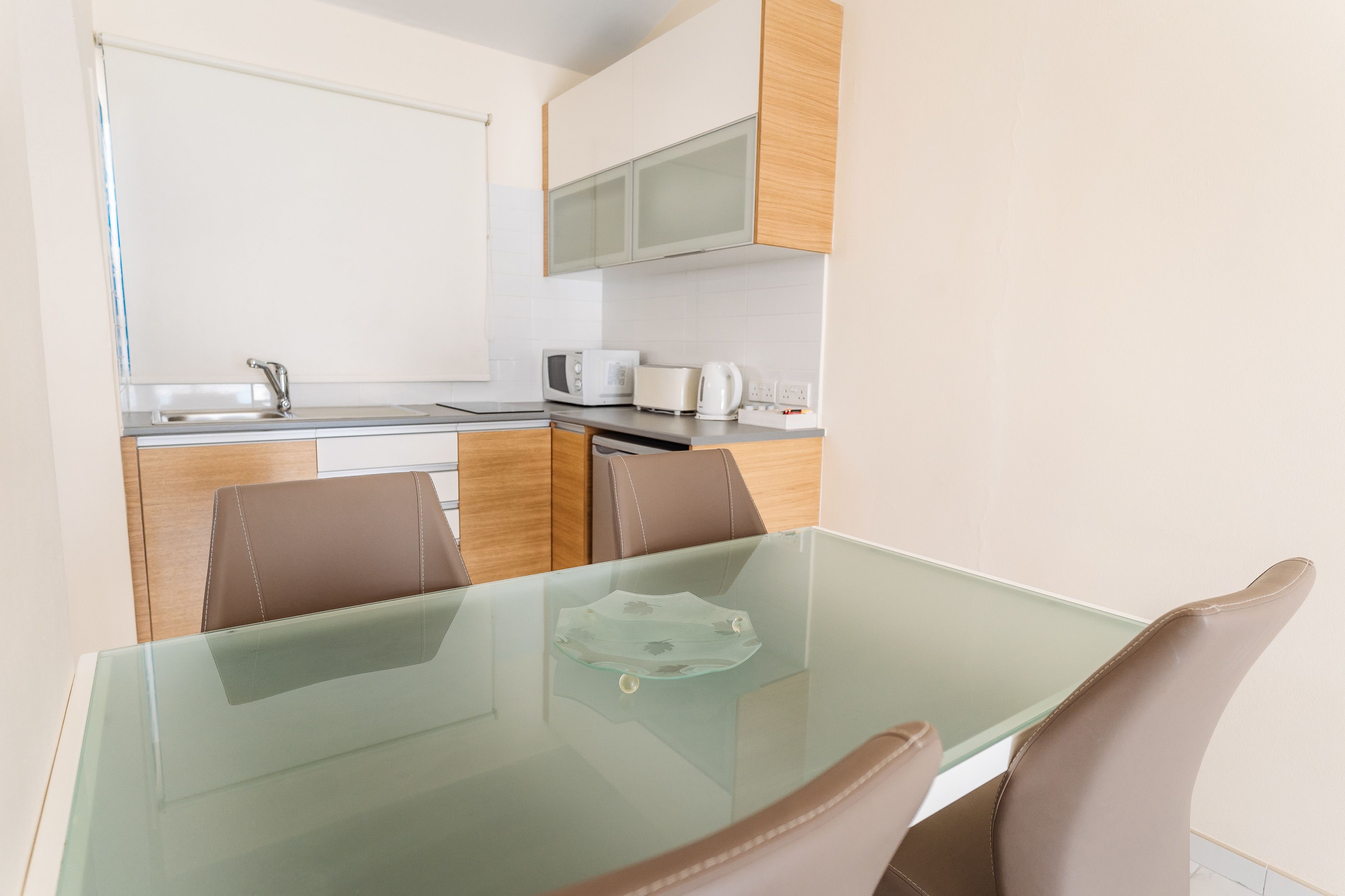 A modern kitchen with a glass-top table and brown chairs, a microwave, toaster, and a sink.