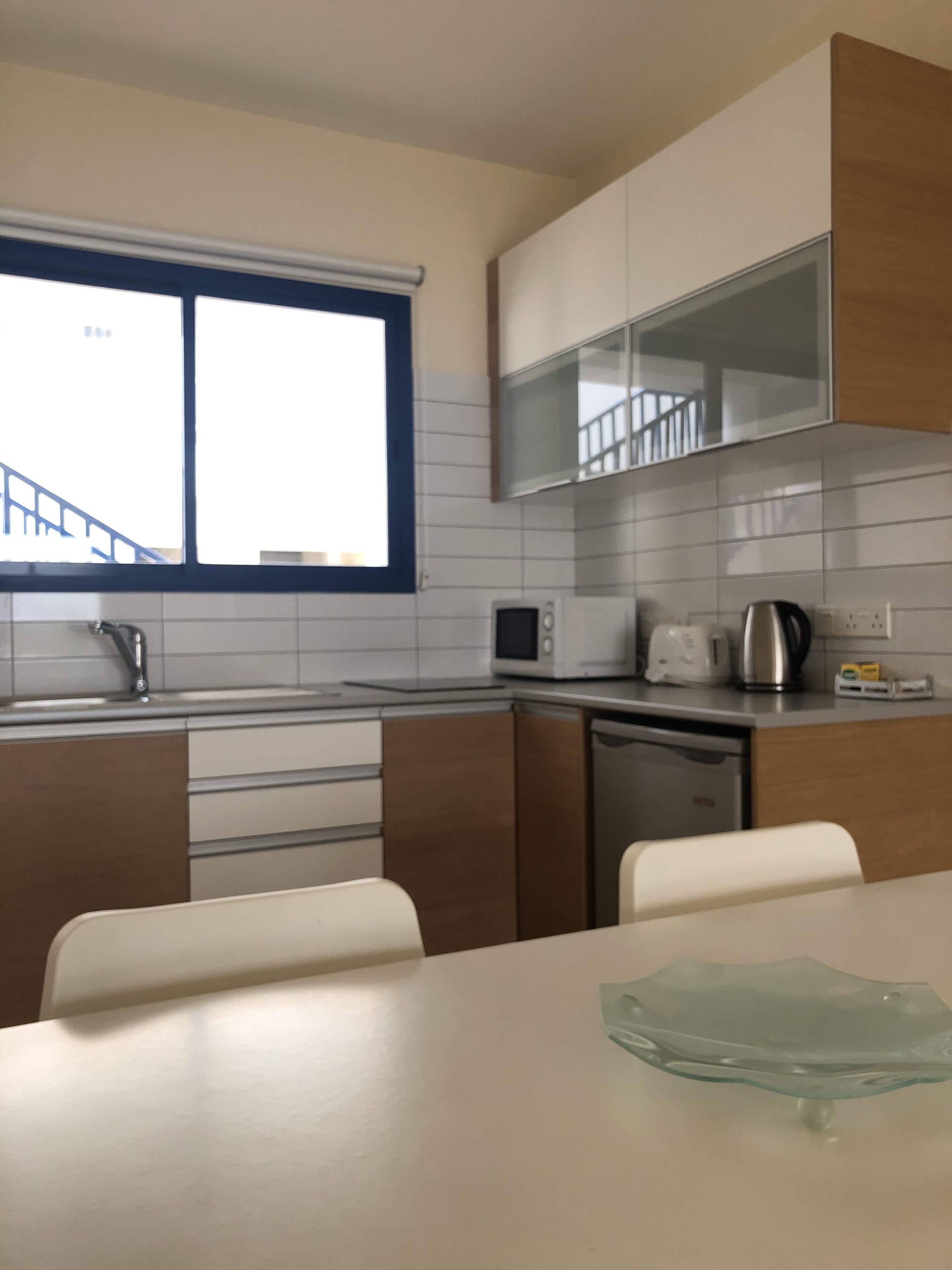 A modern kitchen with white cabinets, a microwave, a kettle, and a dishwasher.