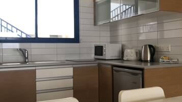 A modern kitchen with white cabinets, a microwave, a kettle, and a dishwasher.