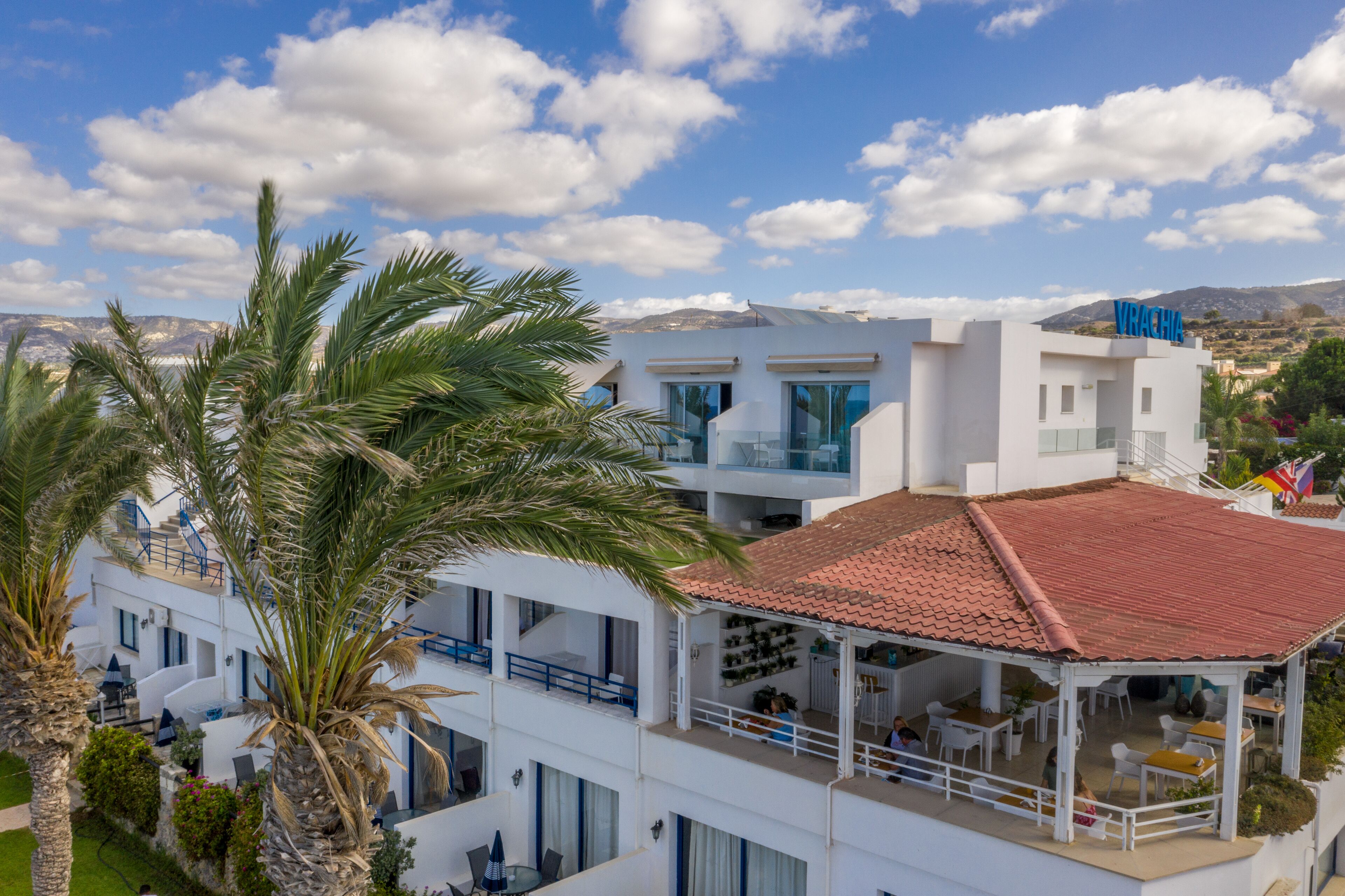 Een modern hotel met een witte gevel, een dak van rode tegels en een balkon met buitenmeubilair.