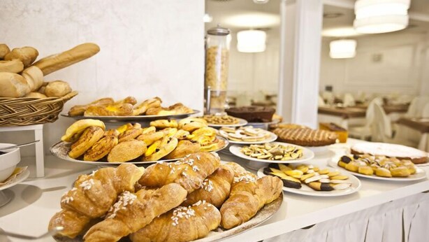 A buffet with various pastries and bread, including croissants and baguettes. - Aurora (Rimini)